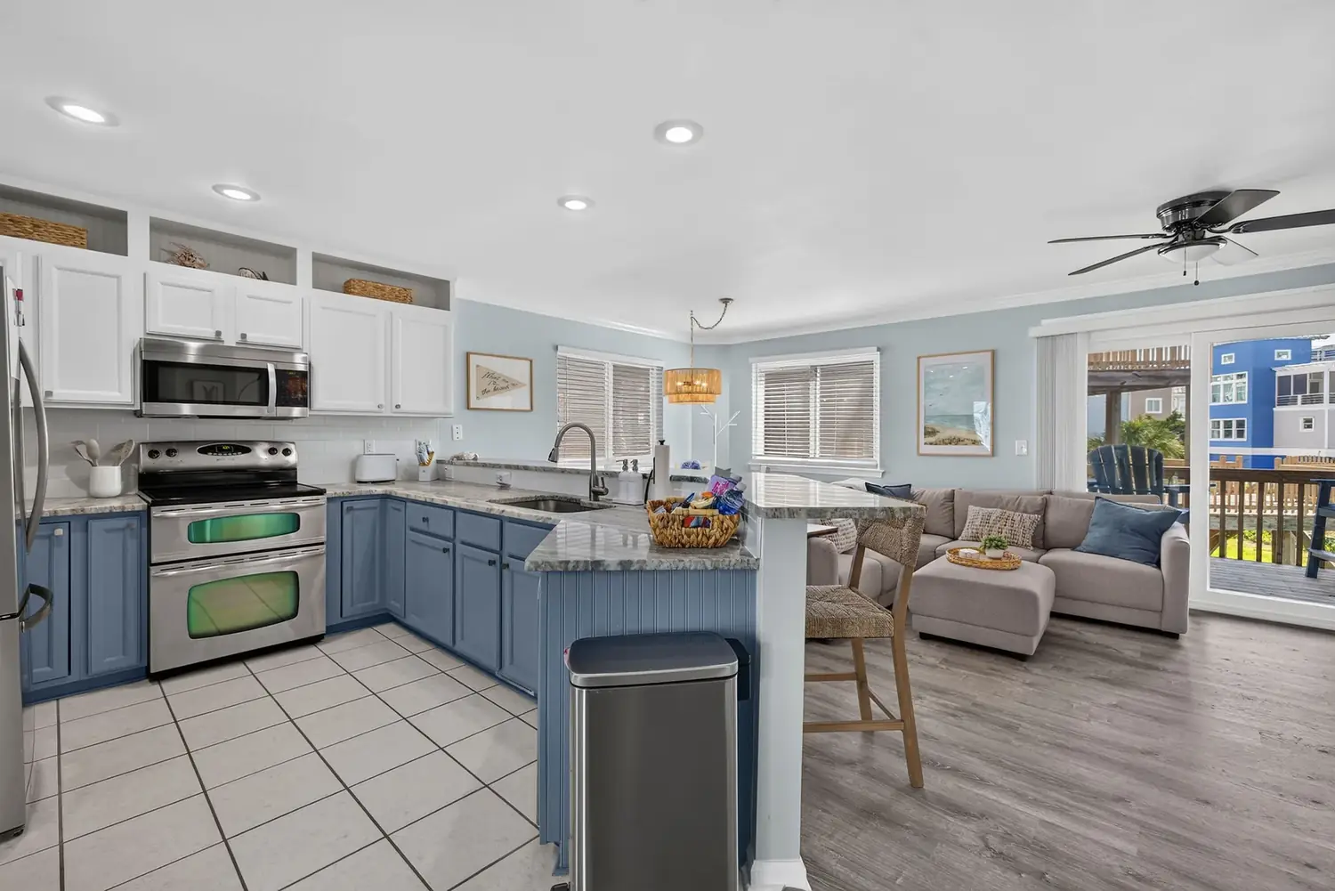 Open kitchen and living room with blue cabinets and a sunny deck beyond